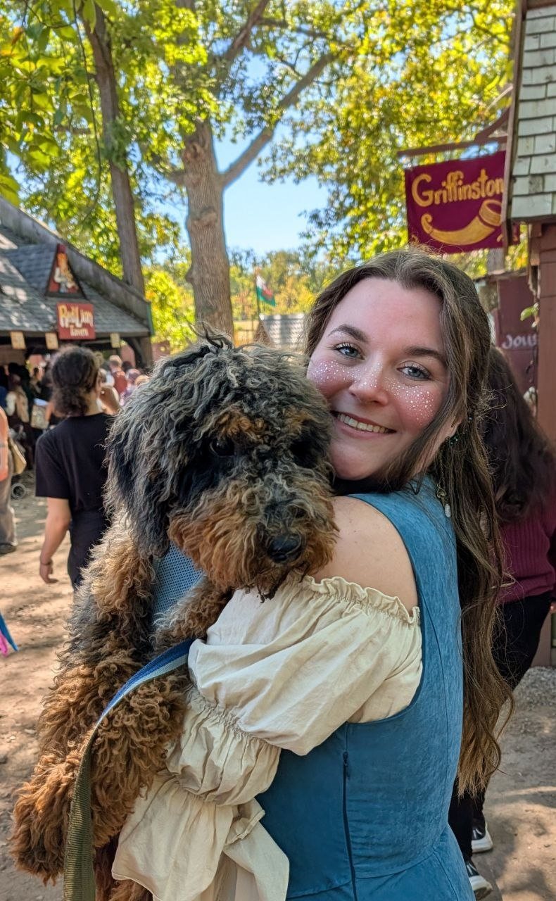 The baker smiling and holding her dog at an outdoor fair