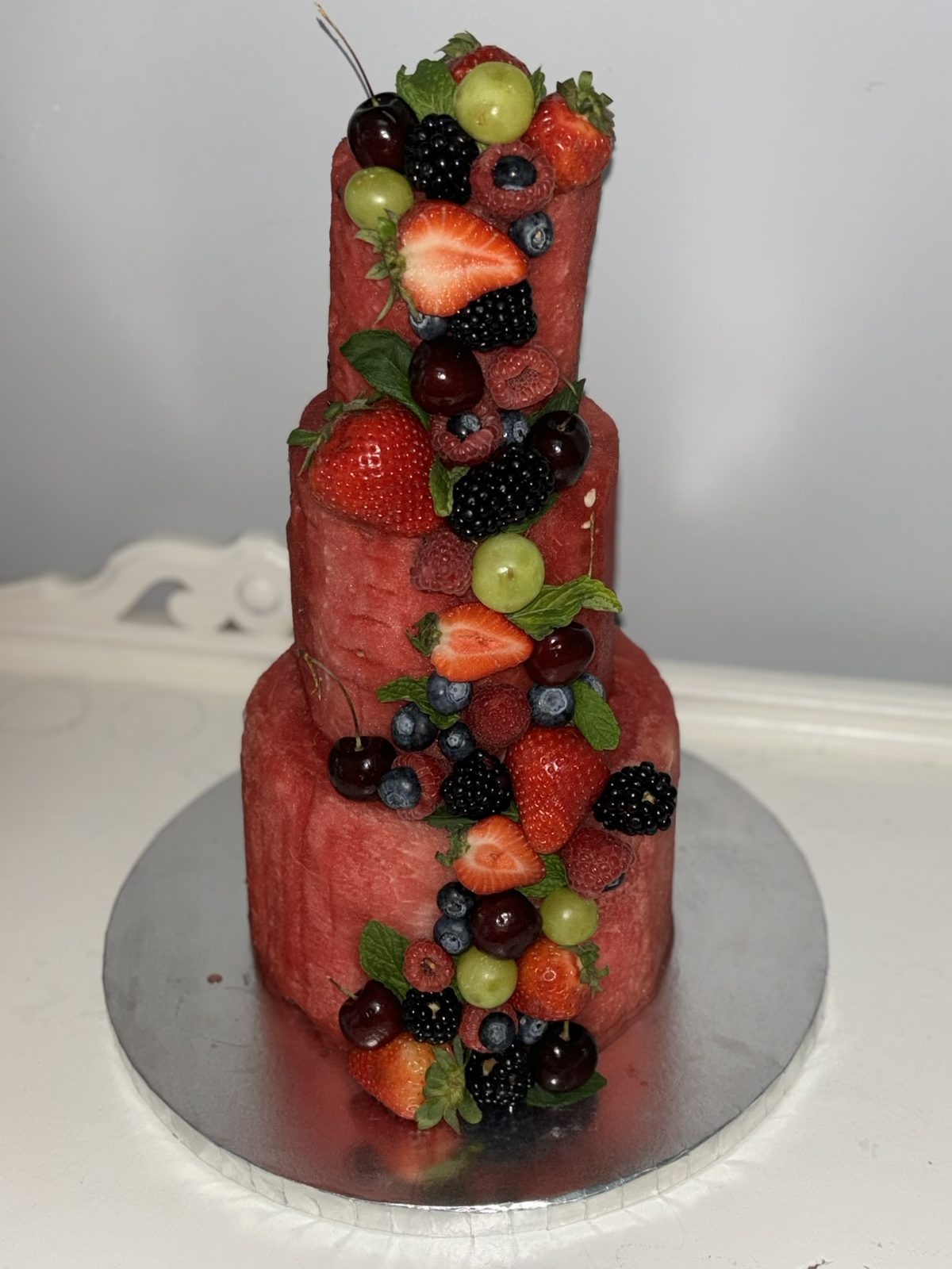 Three-tier watermelon cake stacked with fresh berries and mint